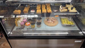 Eine Bäckertheke mit verschiedenen Gebäcken und Desserts, darunter Macarons, Kuchen und Kekse, mit sichtbaren Preisen.