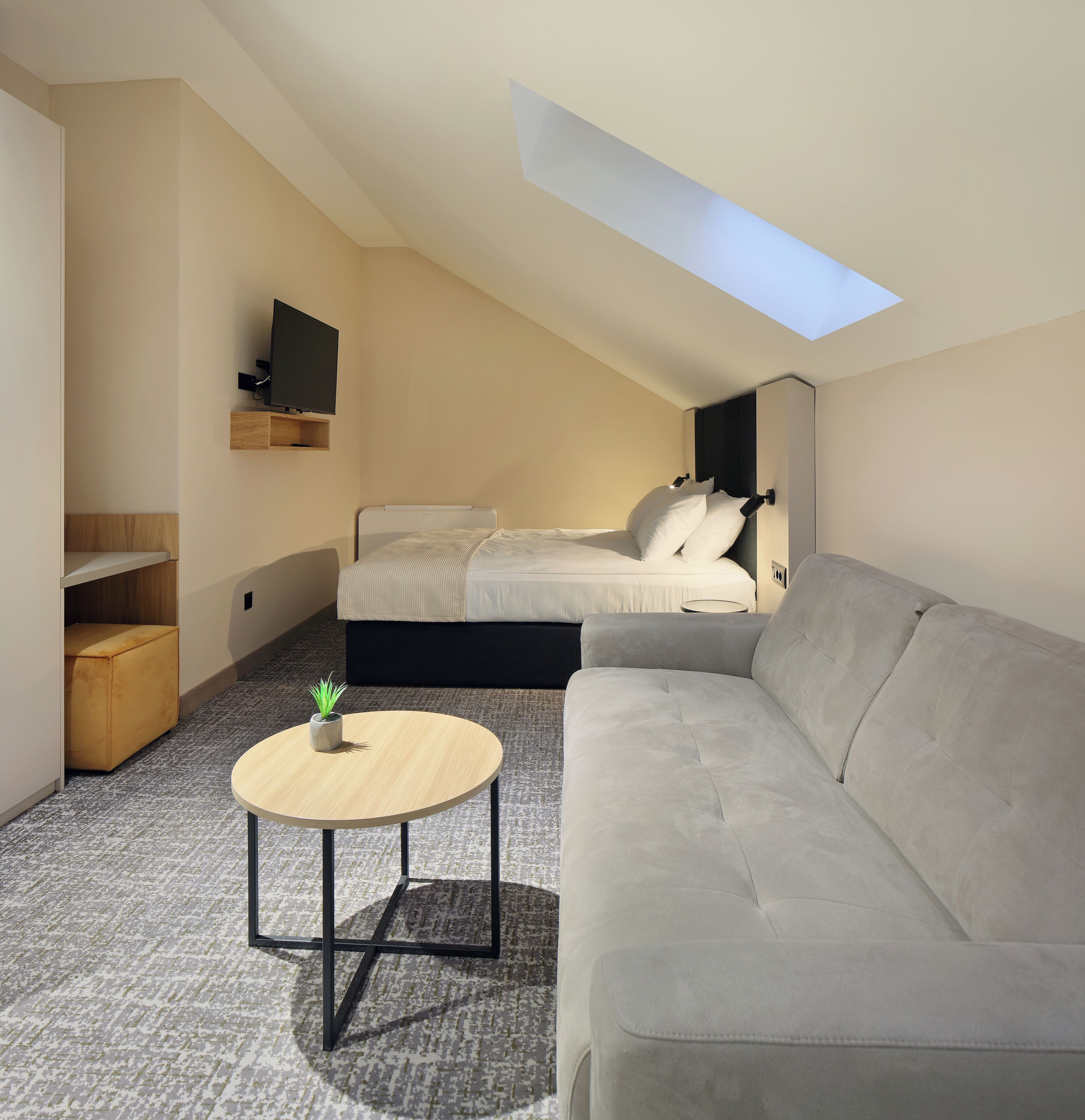 A modern bedroom with a bed, a gray sofa, a small round table, and a skylight.