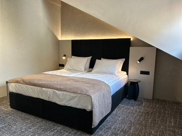 A modern hotel room with a large bed, a headboard with integrated lighting, a bedside table, and a carpeted floor. - Hotel NOVA Inn Sarajevo (Sarajevo)