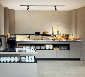 A modern breakfast buffet with a coffee machine, various food items, and a variety of cups and plates. - Hotel NOVA Inn Sarajevo (Sarajevo)