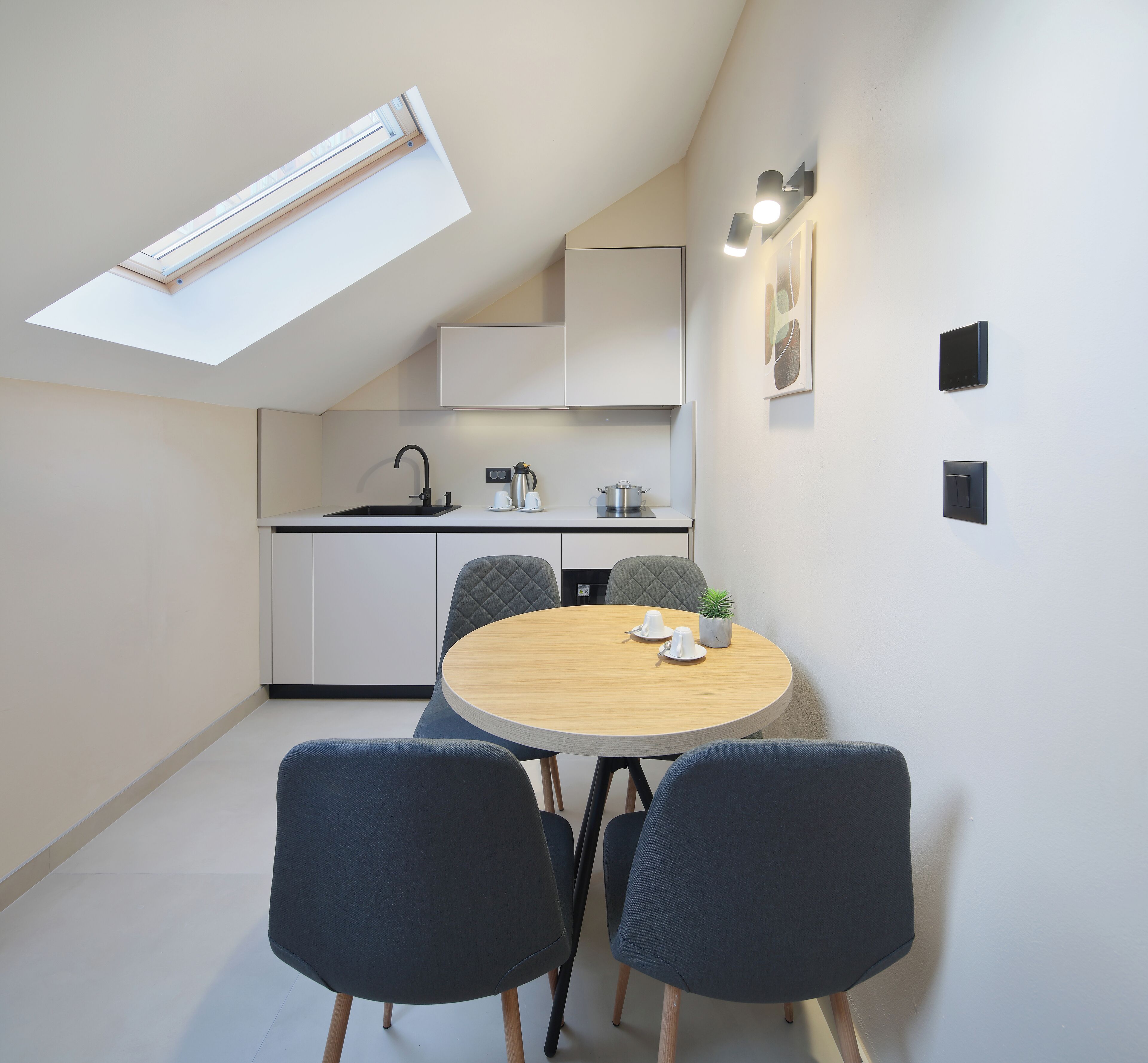 Una cocina compacta con tragaluz, una zona de comedor con dos sillas y una mesa pequeña con tazas y una planta.