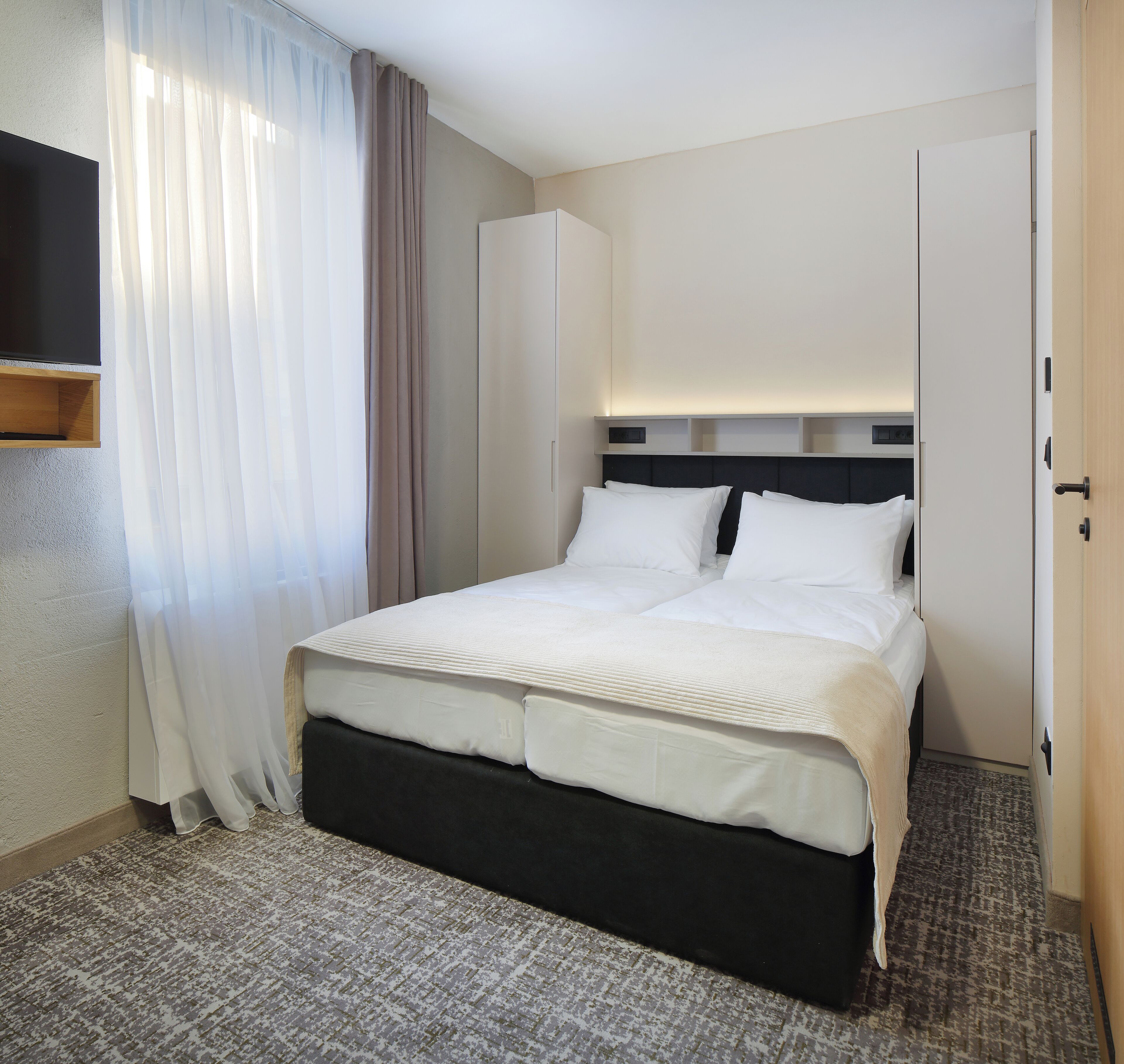 Une chambre d’hôtel avec un lit, un téléviseur fixé au mur et une armoire.