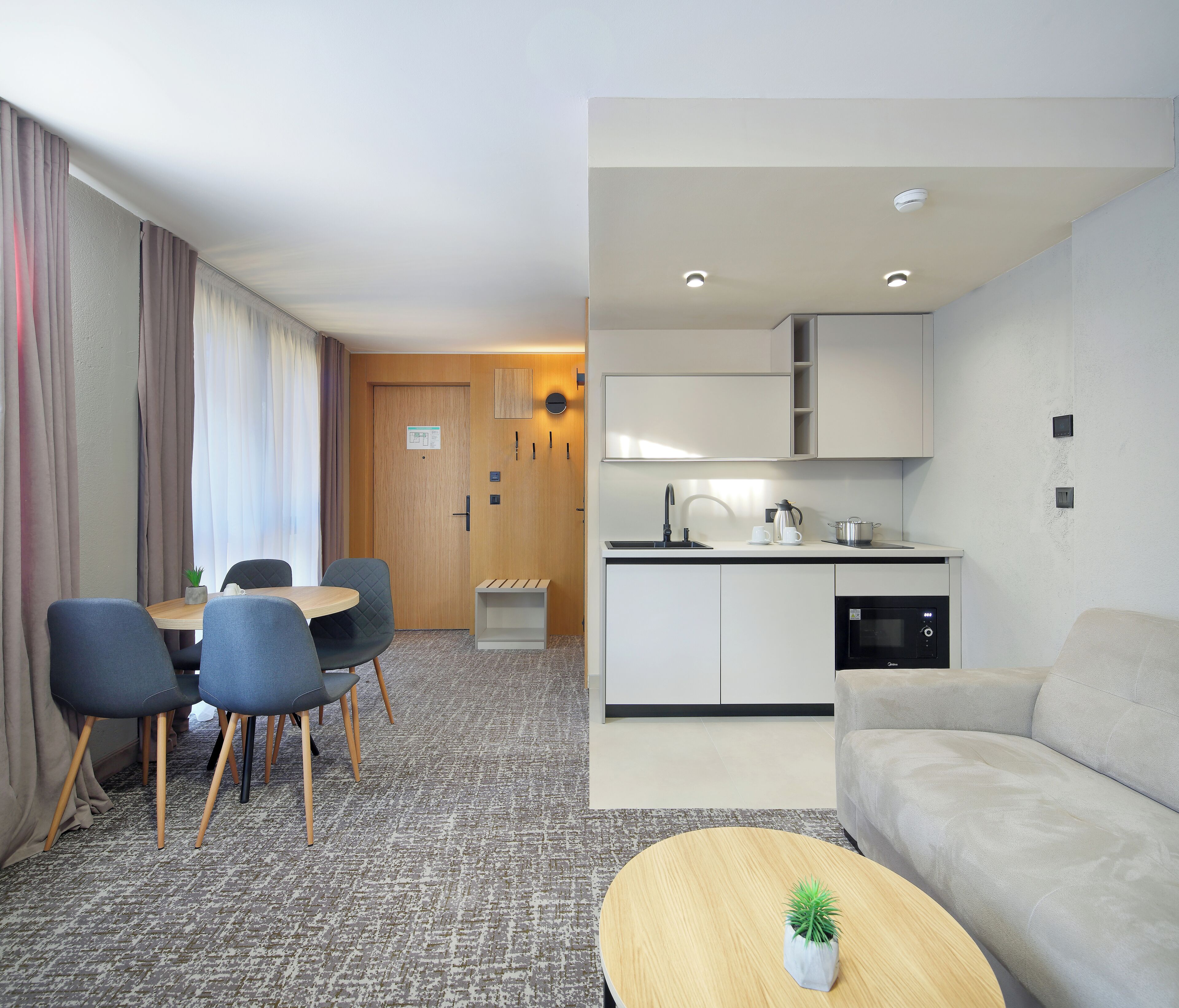 A modern hotel room with a dining area, kitchenette, and a living area.