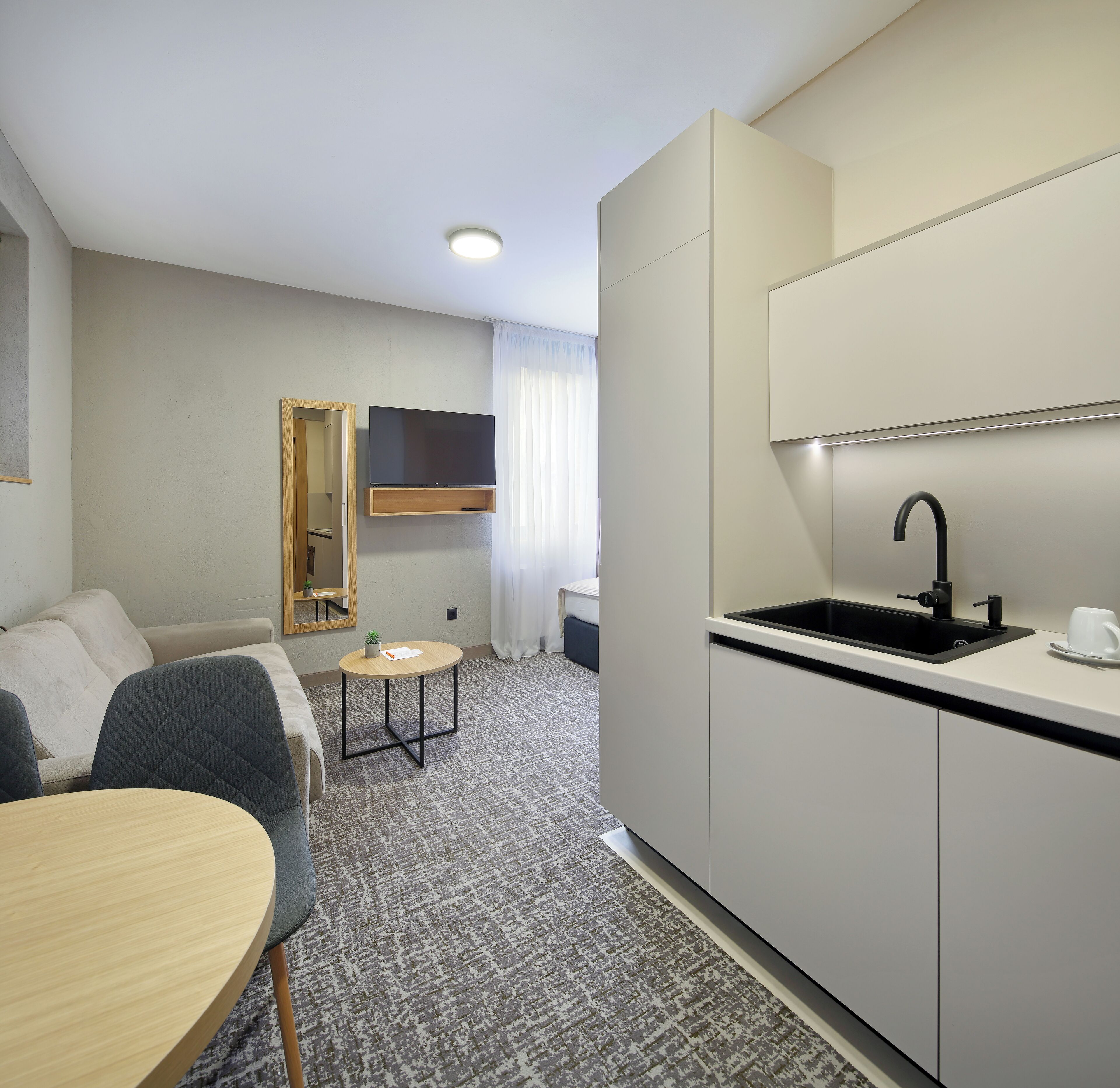 A compact hotel room with a kitchenette, a small dining area, and a seating area.