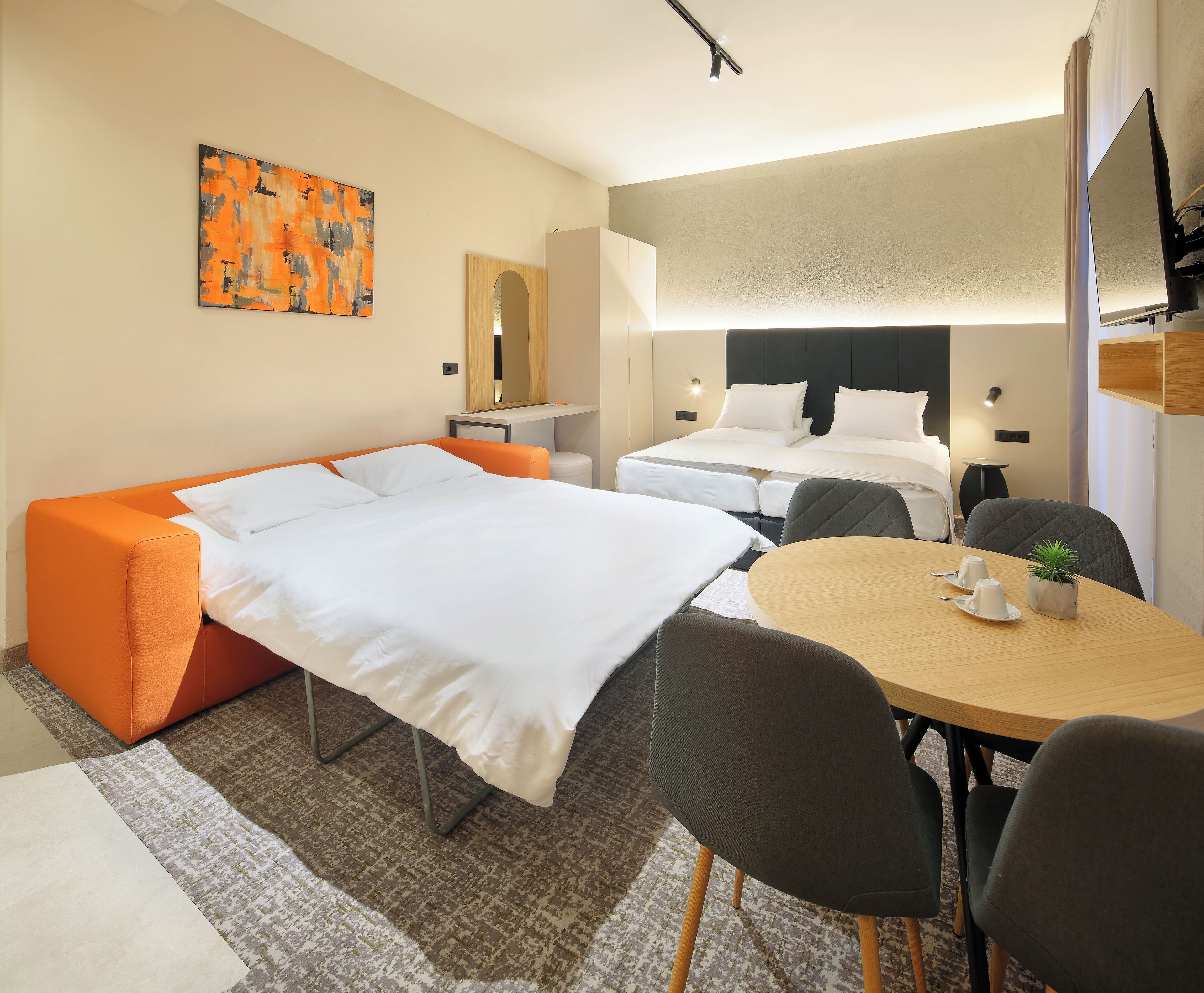 A hotel room with a bed, a sofa, a dining table, and a small plant.