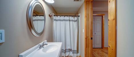 Une salle de bain avec un lavabo blanc, un miroir et un rideau de douche.