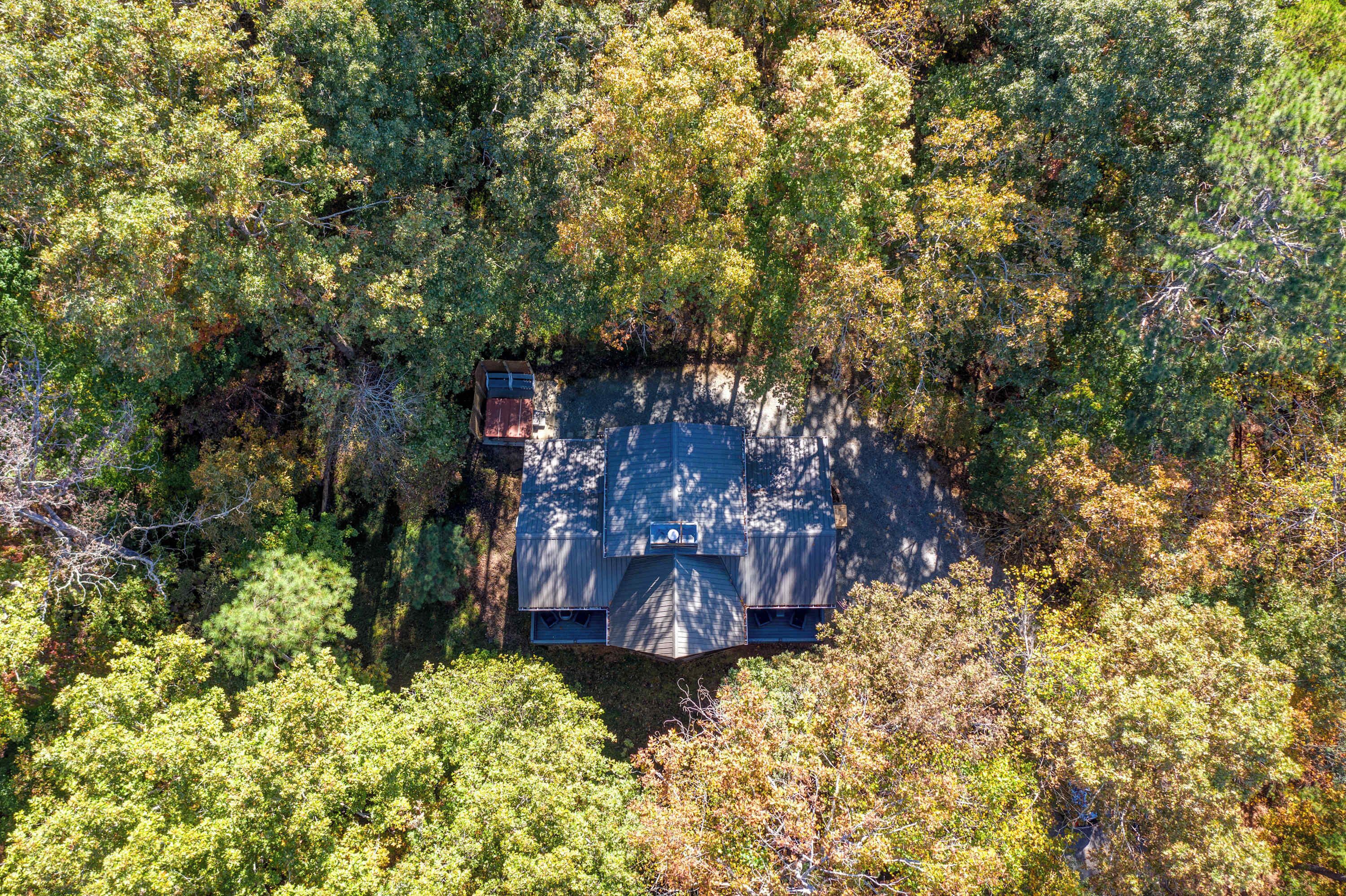 An aerial view of a cabin surrounded by dense forest.