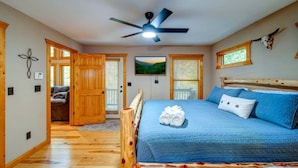 A bedroom with a bed, a ceiling fan, wooden walls, and a window with blinds.
