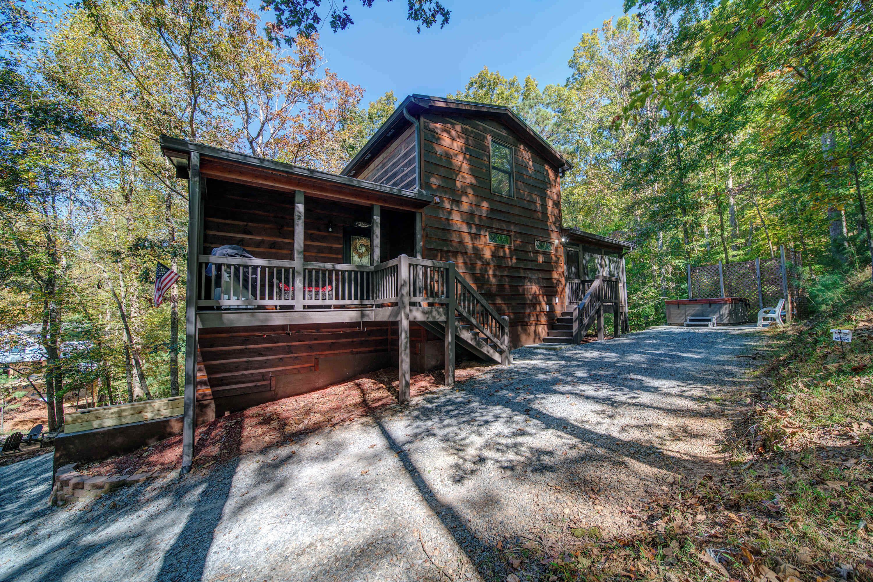 A cabin with a porch, a staircase leading to the main entrance, and a gravel driveway.