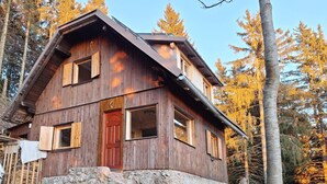 A wooden cabin with a stone foundation, a red door, and multiple windows. - Awesome 4-bedroom Off-Grid Mountain Haven – Hike & Bike Paradise (Tržič)