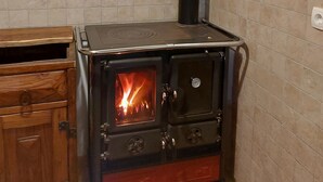 A wood-burning stove with a chimney, a wooden cabinet above it, and a tiled wall. - Awesome 4-bedroom Off-Grid Mountain Haven – Hike & Bike Paradise (Tržič)