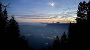 A night view of a mountainous landscape with a crescent moon, silhouetted trees, and distant city lights. - Awesome 4-bedroom Off-Grid Mountain Haven – Hike & Bike Paradise (Tržič)