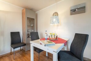 Ein Zimmer mit einem weißen Tisch, zwei Stühlen, einer Lampe, einer Uhr und einem Bild an der Wand.