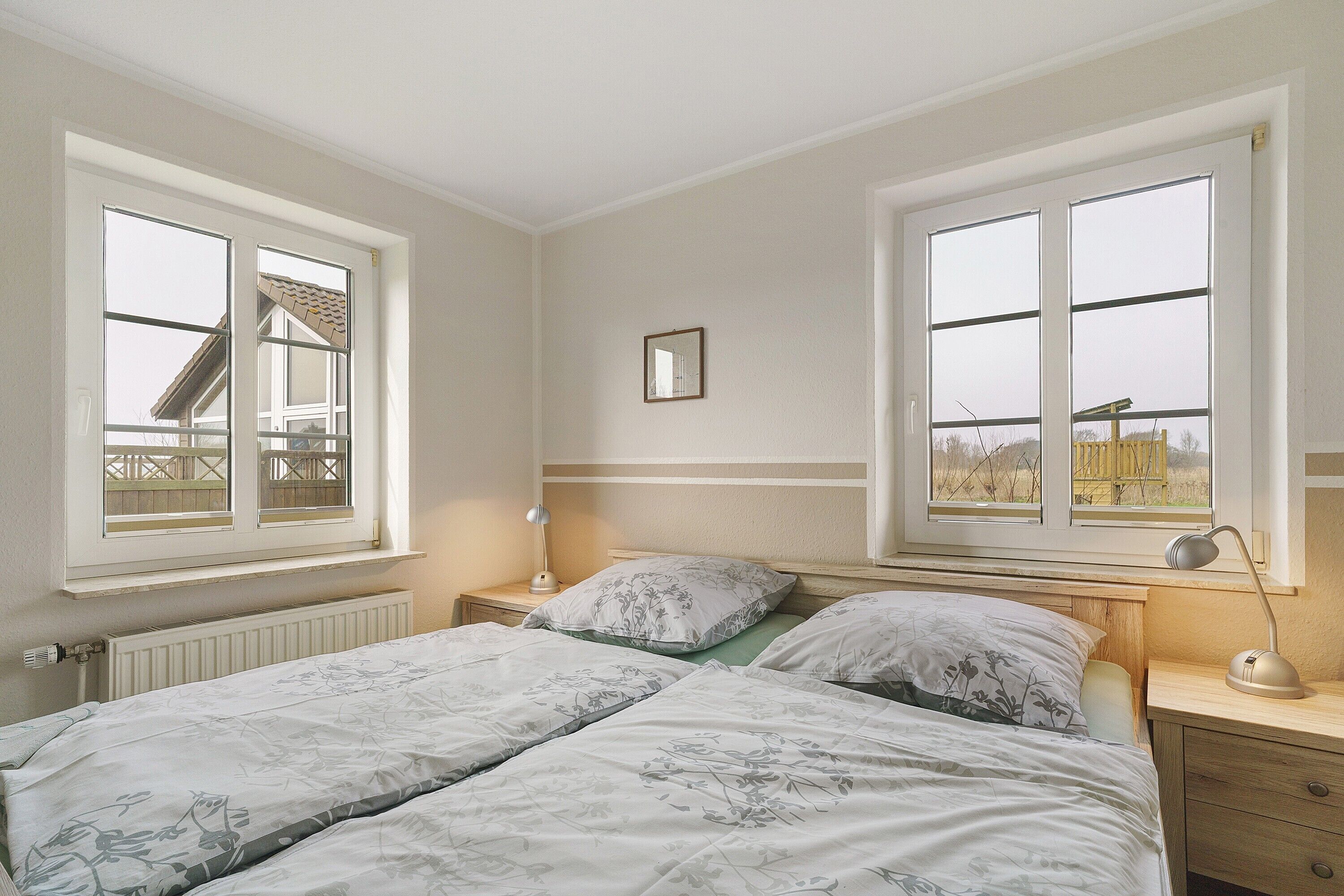 A bedroom with two beds, a window, a bedside table with a lamp, and a radiator.