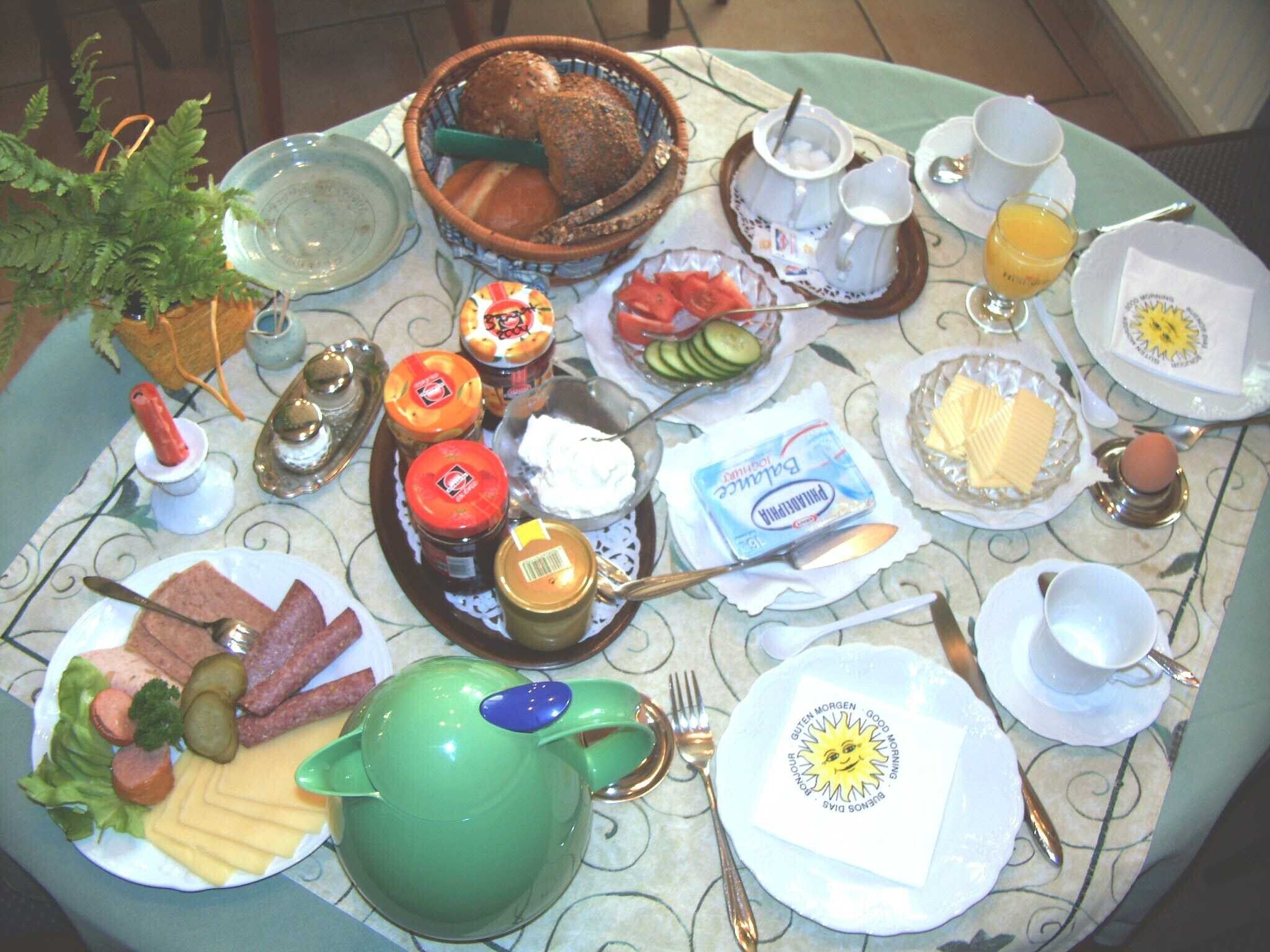 A breakfast table with various food items, utensils, and a green teapot.