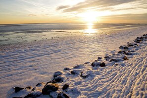 A snowy landscape with a frozen body of water and a row of rocks leading towards the horizon. - Apartment 'Fewo Schütting' with Shared Garden, Balcony and Wi-Fi (Pellworm)