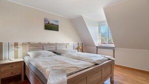 Une chambre à coucher avec un lit en bois, une table de chevet, une lampe de chevet, une fenêtre donnant sur un beau paysage et un tableau accroché au mur.