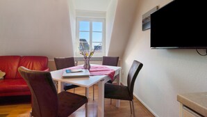 Un coin repas avec une table blanche, une nappe rouge et quatre chaises. Un canapé rouge se trouve à l’arrière-plan.