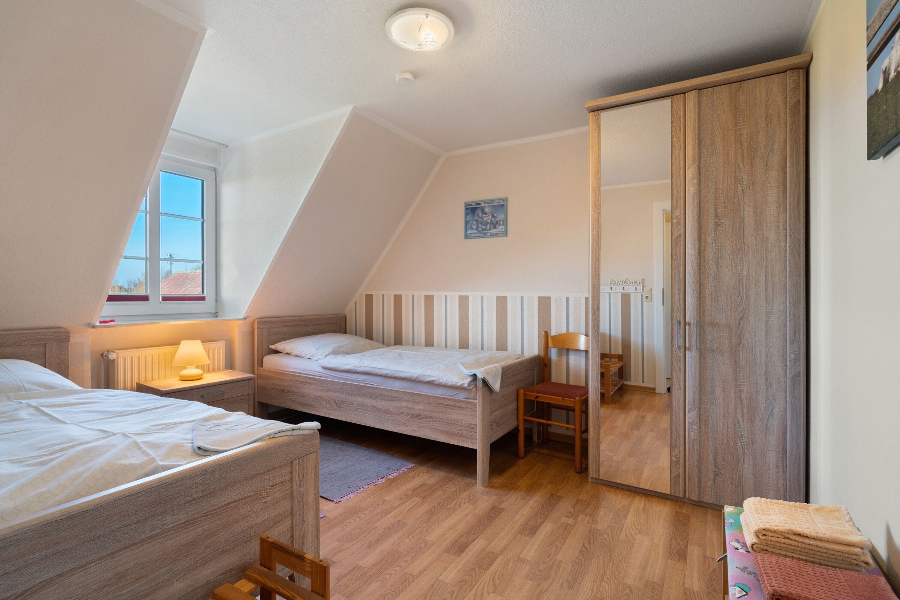 A bedroom with two beds, a wooden wardrobe, a radiator, and a window.