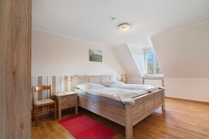 A bedroom with a wooden bed, a nightstand, a chair, a red rug, and a window with a view of greenery. - Apartment 'Fewo Seegarden' with Shared Garden and Wi-Fi (Pellworm)