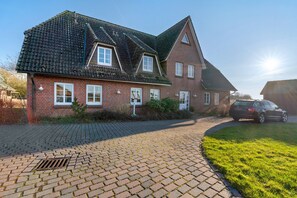 A brick house with a tiled roof, a paved driveway, and a car parked in the driveway. - Apartment 'Fewo Seegarden' with Shared Garden and Wi-Fi (Pellworm)