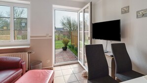 Een kamer met een schuifdeur naar een tuin, een televisie aan de muur en twee stoelen.