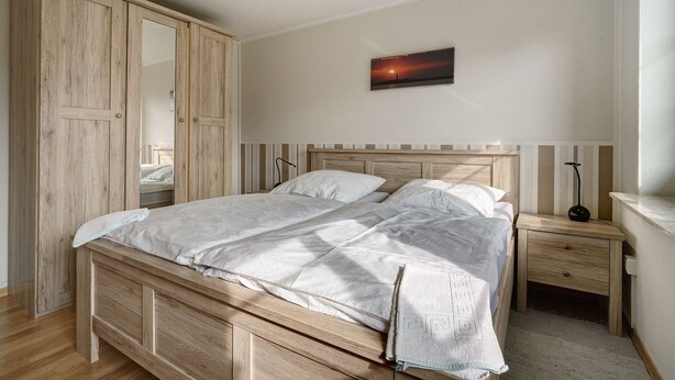 Een slaapkamer met een houten bed, nachtkastje, bedtafel en een kledingkast.