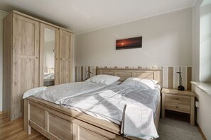 A bedroom with a wooden bed, a nightstand, a bedside table, and a wardrobe. - Apartment 'Fewo Waldhusen' with Shared Garden, Balcony and Wi-Fi (Pellworm)