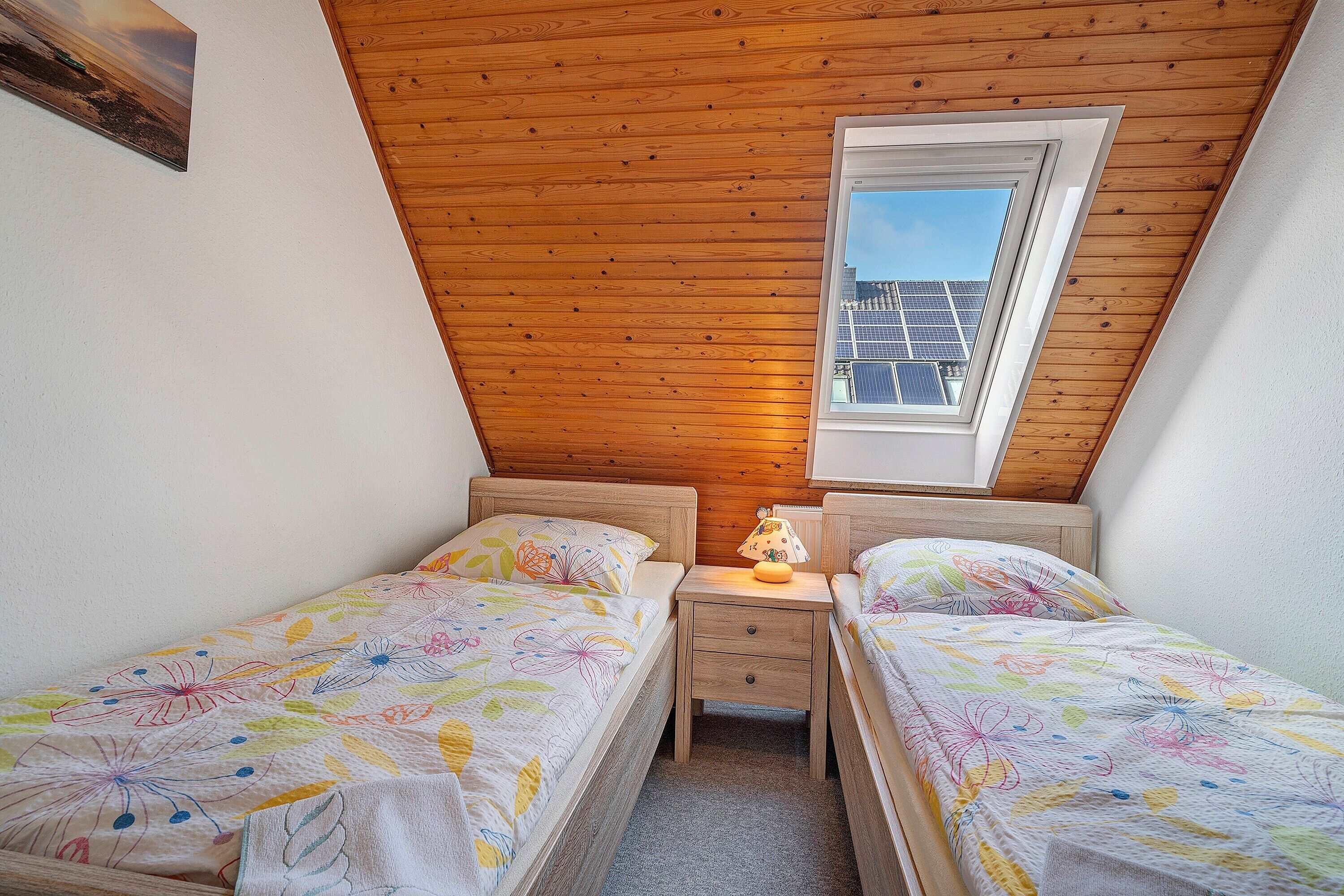 A bedroom with two beds, a nightstand, a window, and a wooden ceiling.