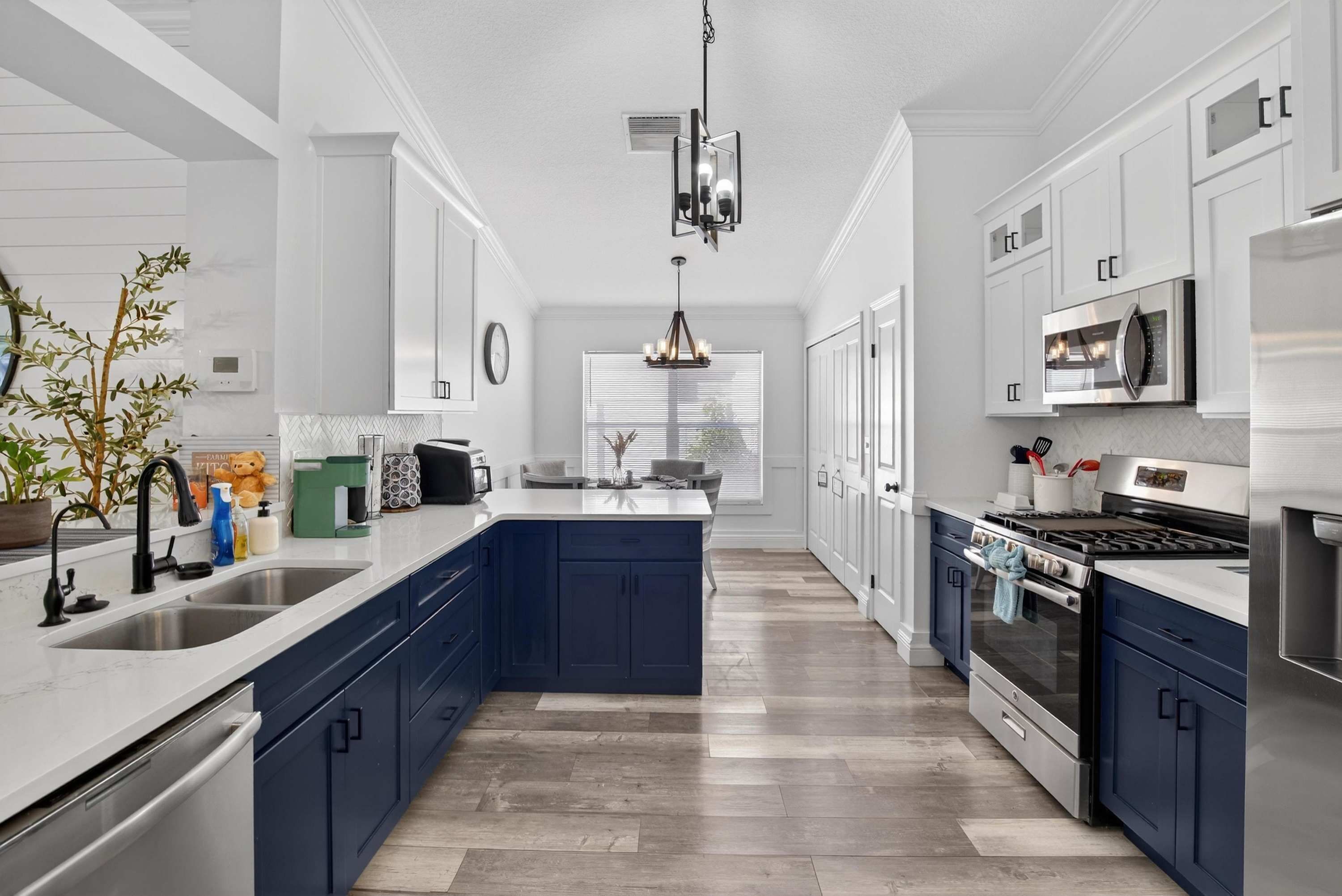 Una cocina moderna con armarios blancos, una isla central, electrodomésticos de acero inoxidable y una lámpara colgante.