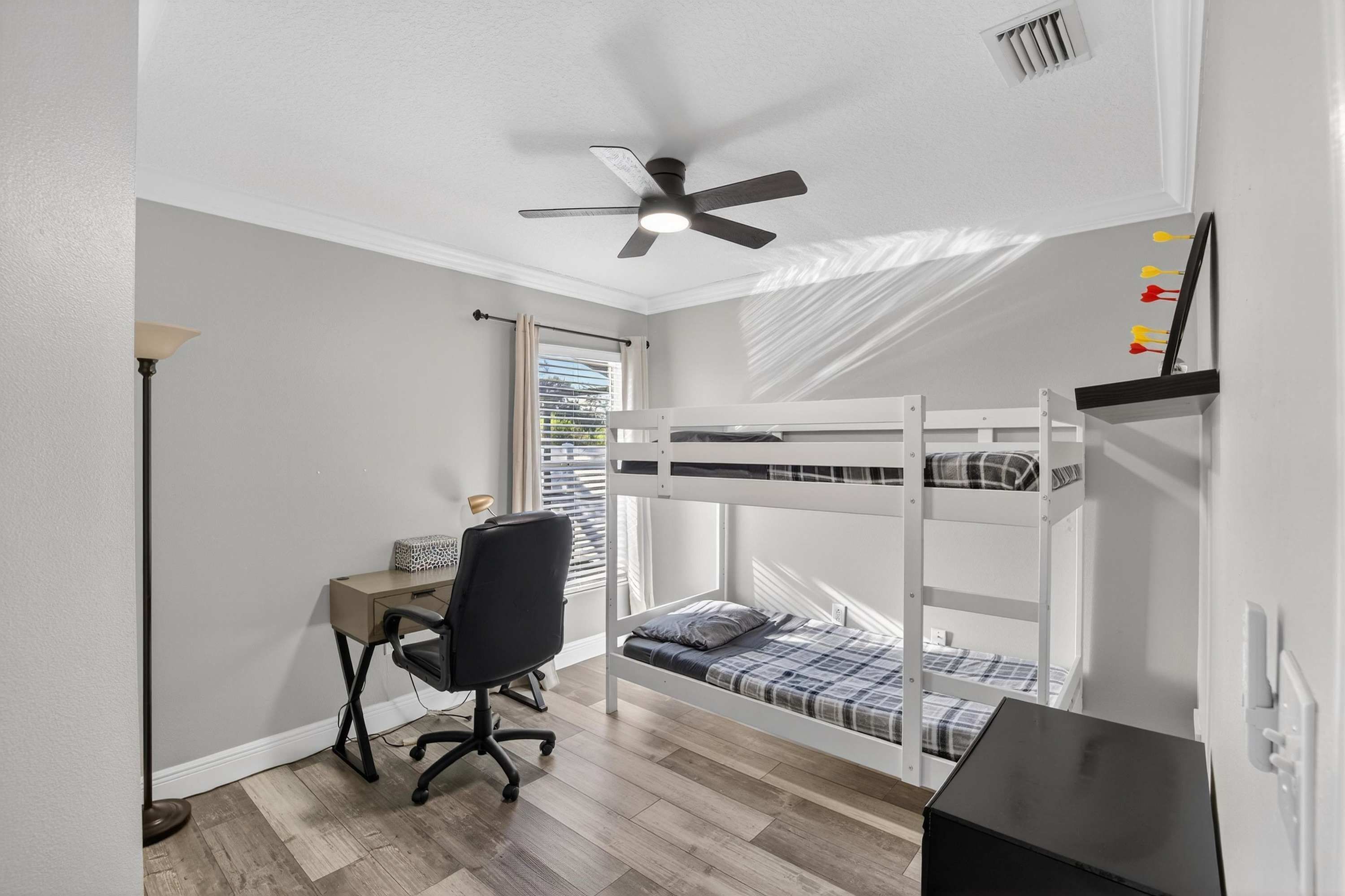 A bedroom with a bunk bed, a desk with a chair, a ceiling fan, and a window with blinds.