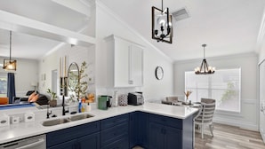 A modern kitchen with dark blue cabinets, white countertops, and a large island. There are various appliances and decorative items on the countertops. - Lakefront 4-bedroom Home With Pool (Brandon)