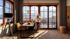 A room with a large window overlooking a snowy landscape, a dining table with chairs, and a tripod-mounted camera. - Karpielówka Suites Parking & Mountain View by Downtown Apartments (Kościelisko)