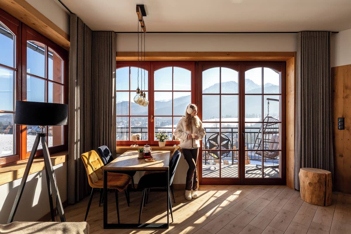 Une pièce dotée d’une grande fenêtre donnant sur un paysage enneigé, une table à manger avec des chaises et un appareil photo fixé sur un trépied.