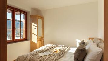 Une chambre avec une grande fenêtre, une armoire en bois, un lit avec une couverture et des oreillers, et un livre posé sur le lit.
