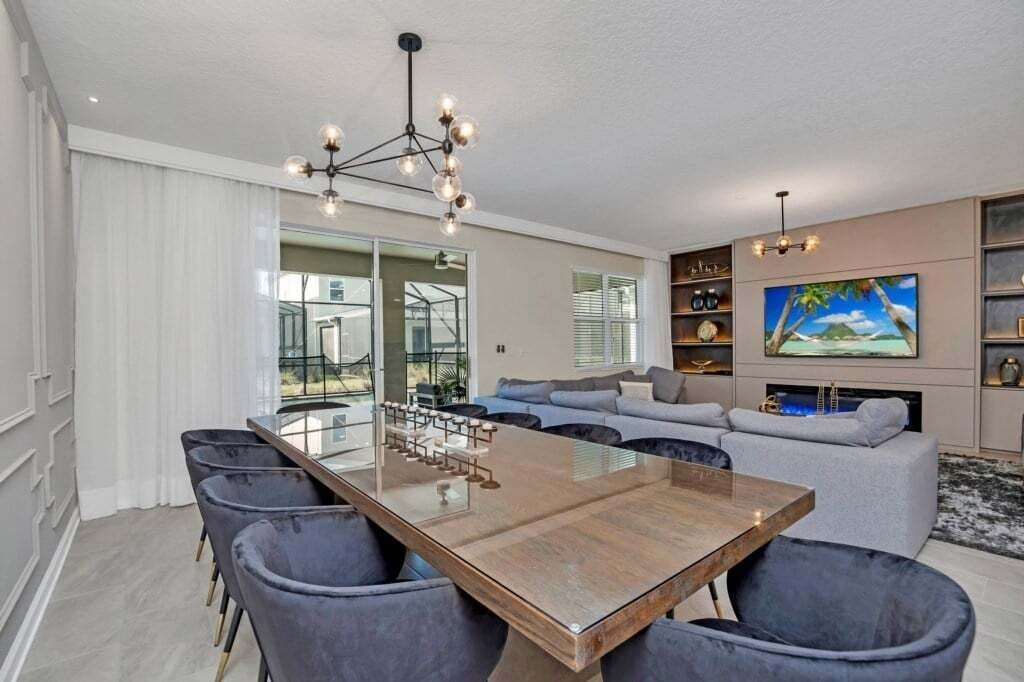 Una sala de estar moderna con una gran mesa de comedor de madera, sofás grises y una araña.
