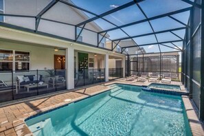 A pool area with a glass-enclosed patio, lounge chairs, and a clear view of the sky. - 9 Bedroom With Everything For Happiness! 9 Home (Kissimmee)
