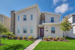 A modern two-story residential building with a stone facade, a red door, and a well-maintained lawn with small shrubs. - 9 Bedroom With Everything For Happiness! 9 Home (Kissimmee)