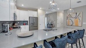 A modern kitchen with white cabinets, a large island, and bar stools. - 9 Bedroom With Everything For Happiness! 9 Home (Kissimmee)