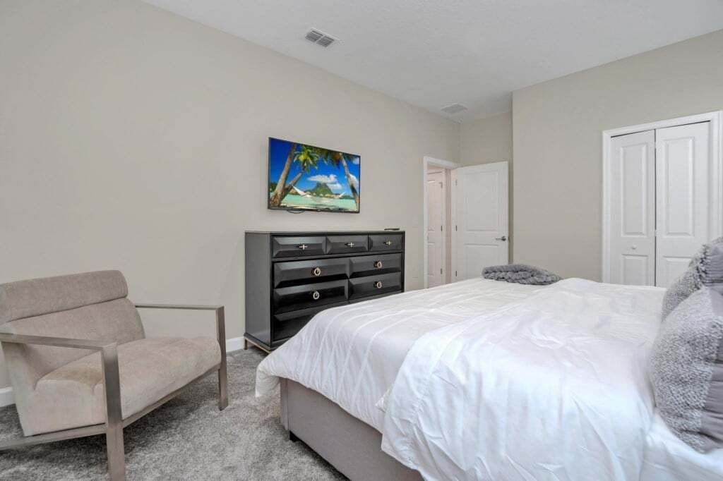 A bedroom with a bed, a chair, a dresser, and a door.