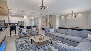 A modern living room with a grey sofa, a coffee table, and a chandelier. - 9 Bedroom With Everything For Happiness! 9 Home (Kissimmee)