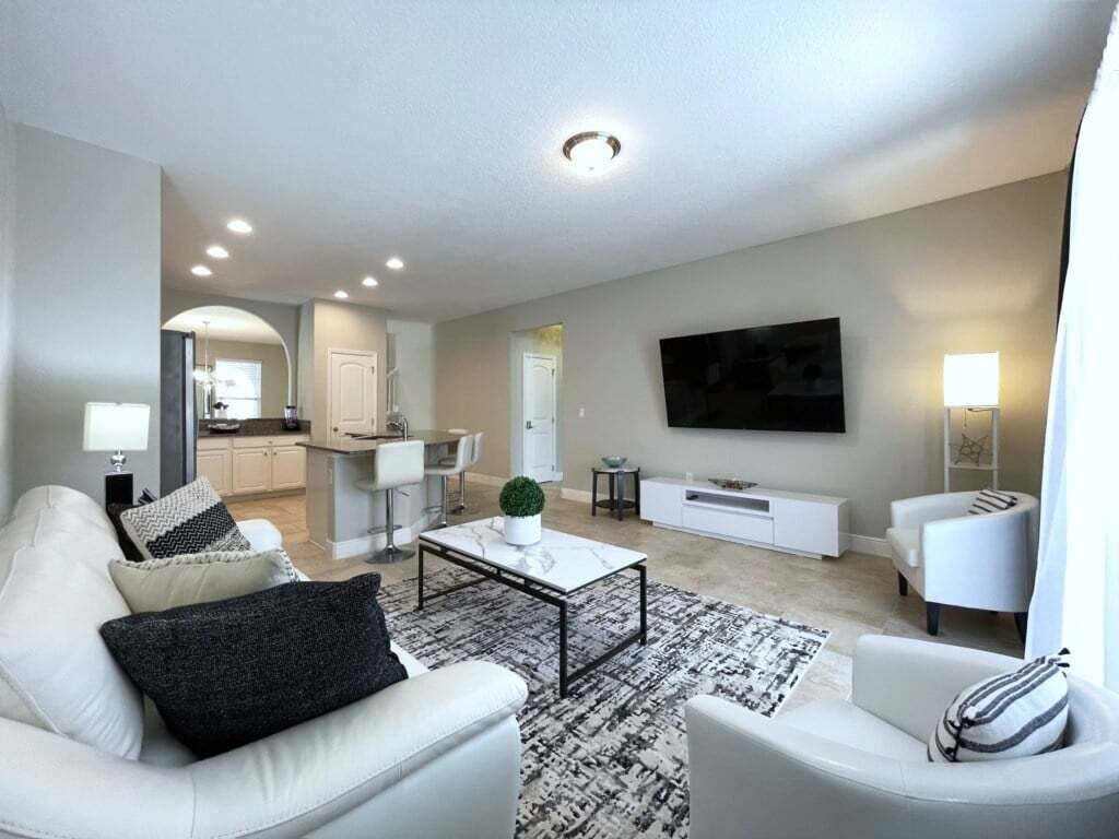 A modern living room with a sofa, armchair, coffee table, and TV. There is a kitchen in the background.
