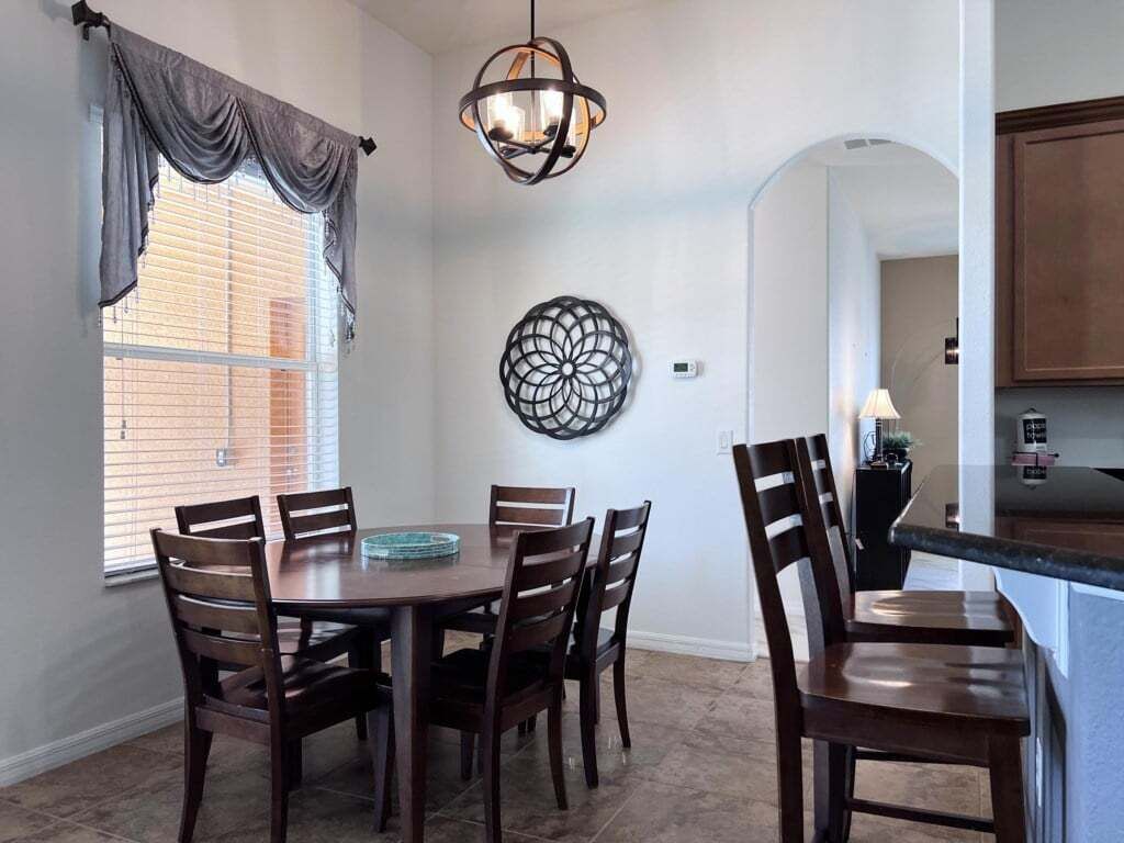 Un comedor con una mesa redonda, seis sillas, una araña y un elemento decorativo en la pared.