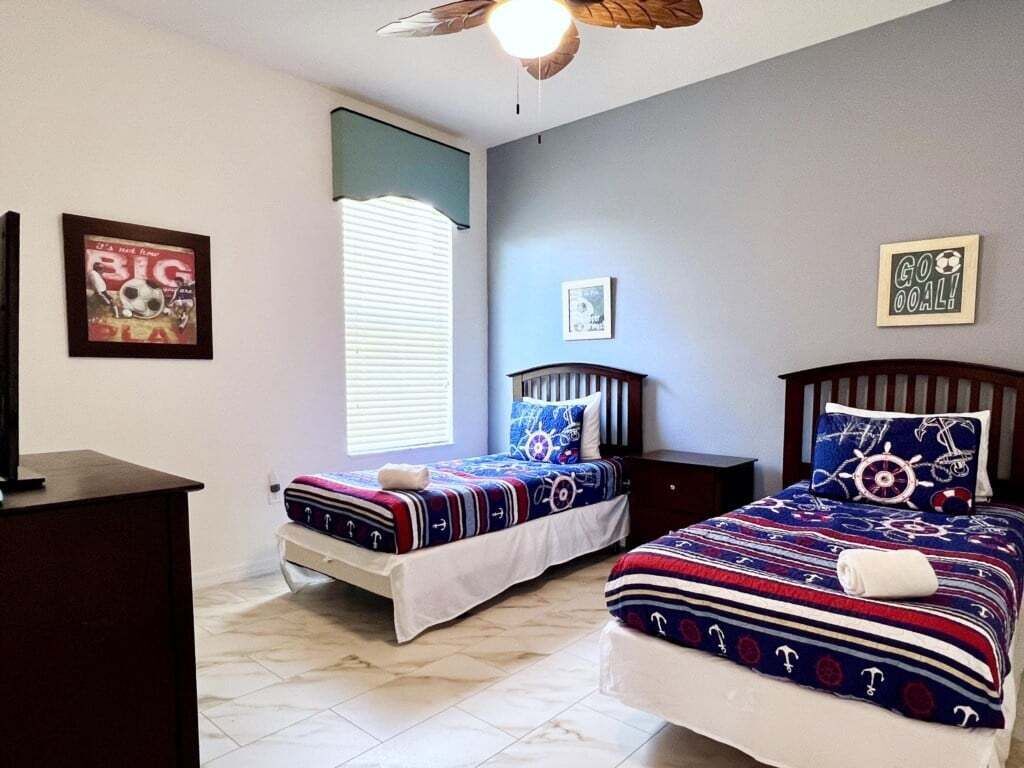 A bedroom with two beds, a ceiling fan, and a window with blinds.