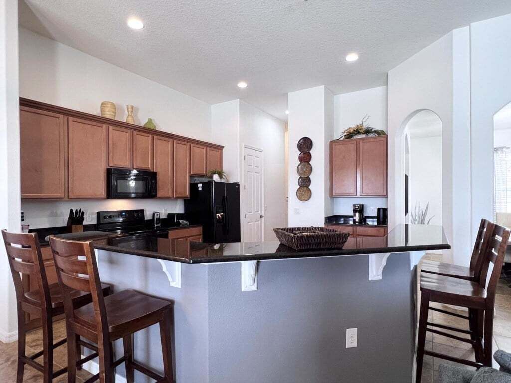 A modern kitchen with wooden cabinets, a black refrigerator, and a central island with bar stools.