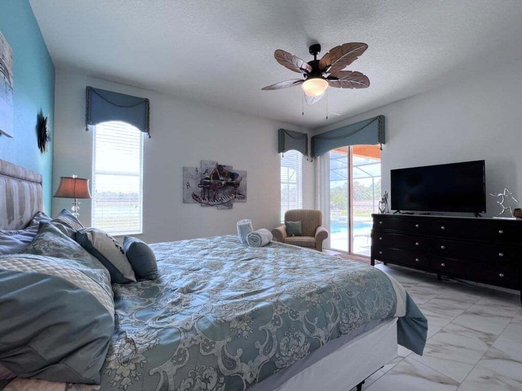 A bedroom with a bed, a ceiling fan, a TV, a dresser, and a chair.