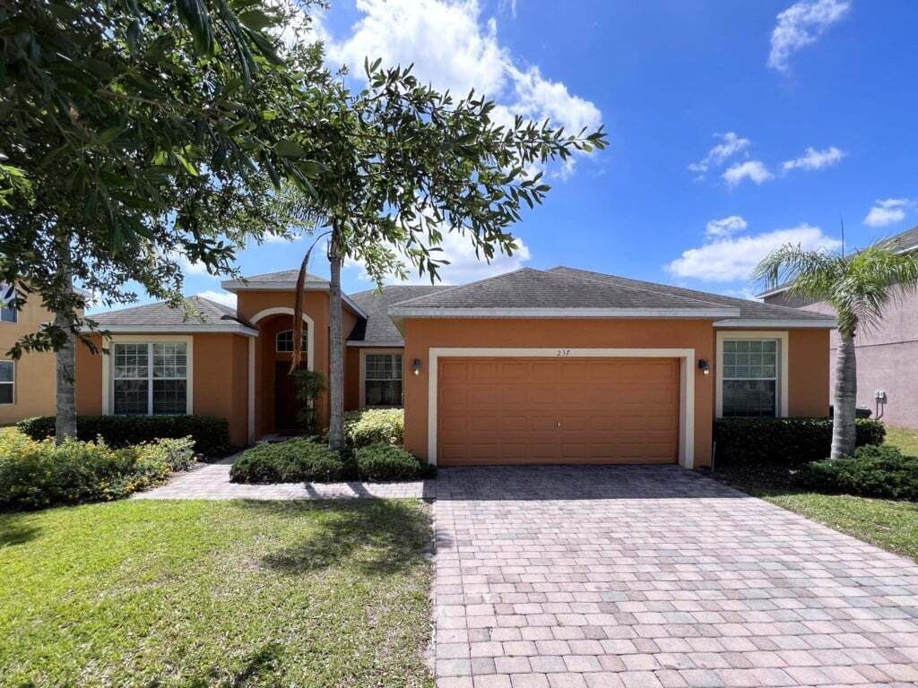 A two-story house with a garage, a brick driveway, and a well-maintained lawn.