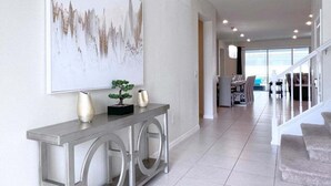 A modern interior with a console table, a large abstract painting, and a staircase leading to another area. - Luxury & Loaded Pool Home With Private Pool 8 Bedroom Home (Davenport)