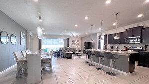A modern kitchen with dark cabinets, a central island, and pendant lighting. - Luxury & Loaded Pool Home With Private Pool 8 Bedroom Home (Davenport)