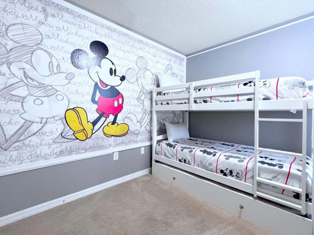A child's room with a Mickey Mouse mural, bunk beds, and a grey wall.
